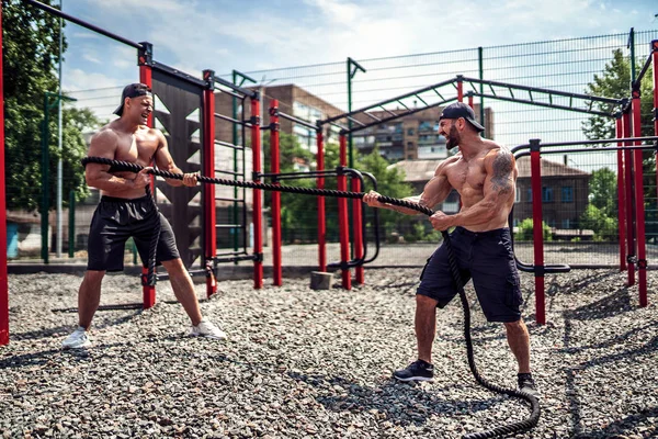 Los hombres trabajan duro con cuerda en el patio del gimnasio de la calle. Fuerza y motivación. Entrenamiento al aire libre. fitness, deporte, ejercicio, entrenamiento y concepto de estilo de vida  . — Foto de Stock