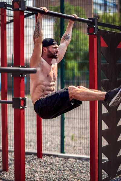 夏の公園で水平バーで腹部運動をしている強い筋肉ひげの男。フィットネス、スポーツ、エクササイズ、トレーニング、ライフスタイルの概念. — ストック写真