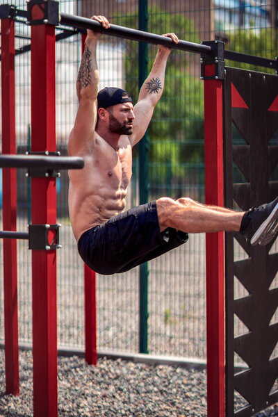 Strong Muscular bearded man doing abdominal exercise on horizontal bar in summer park. fitness, sport, exercising, training and lifestyle concept.