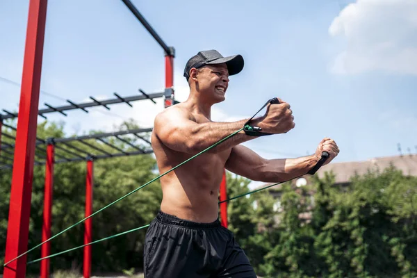 Fitness-Mann trainiert Brust mit Widerstandsbändern auf Straße Turnhalle Hof. Outdoor-Training. Körpertraining mit Geräten draußen. Zubehör aus Gummiband. — Stockfoto