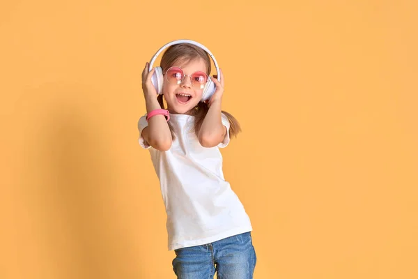 Girl listening to music in headphones on yellow background. Cute child enjoying happy dance music on studio background wall — Stock Photo, Image