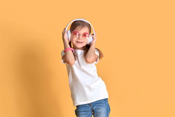 Girl listening to music in headphones on yellow background. Cute child enjoying happy dance music on studio background wall — Stock Photo, Image