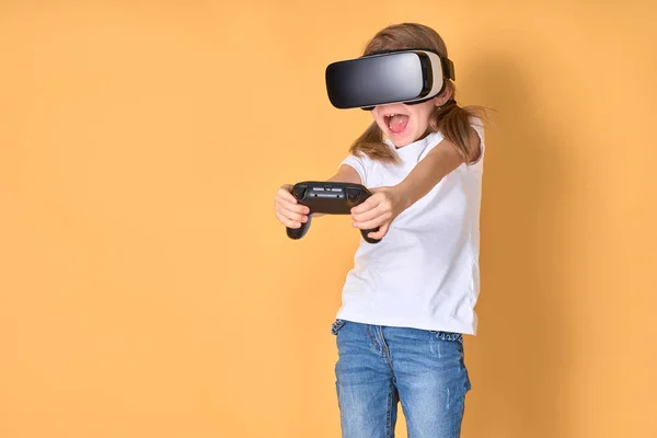 Menina experimentando VR headset vs joystick jogo no fundo amarelo. Emoções surpreendentes no rosto dela. Criança usando um gadget de jogo para realidade virtual . — Fotografia de Stock