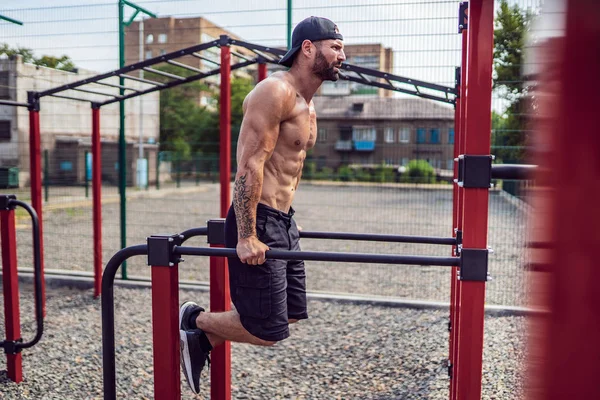 Starker muskulöser Mann macht Liegestütze auf unebenem Stufenbarren in Outdoor-Street-Gym — Stockfoto