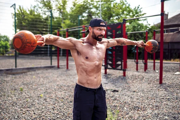 Sportlicher Mann beim Training mit einer Kettlebell auf dem Hof der Turnhalle. Stärke und Motivation. — Stockfoto