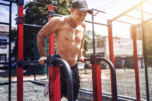 Strong muscular man doing push-ups on uneven bars in outdoor street gym — Stock Photo, Image