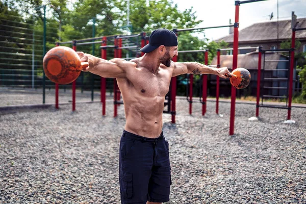 Sportlicher Mann beim Training mit einer Kettlebell auf dem Hof der Turnhalle. Stärke und Motivation. — Stockfoto