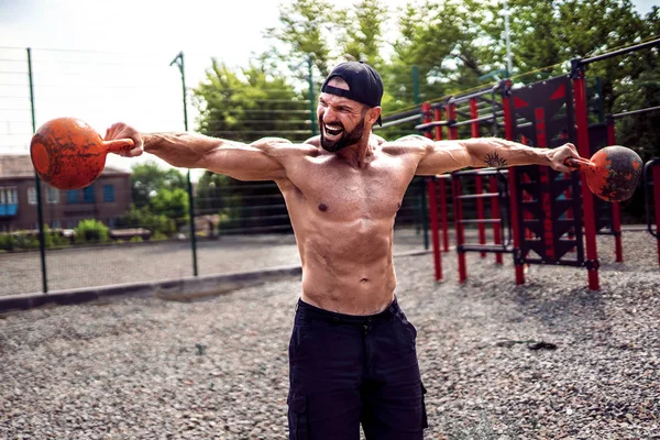 Sportlicher Mann beim Training mit einer Kettlebell auf dem Hof der Turnhalle. Stärke und Motivation. — Stockfoto