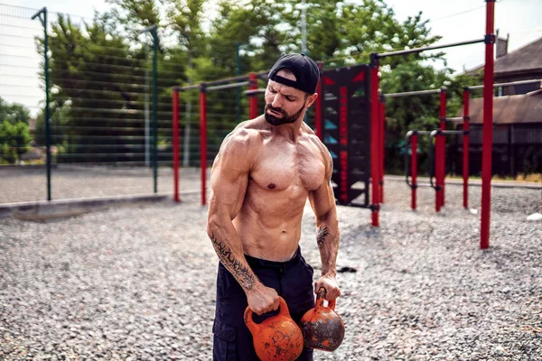 Hombre atlético haciendo ejercicio con un kettlebell en el patio del gimnasio callejero. Fuerza y motivación . —  Fotos de Stock