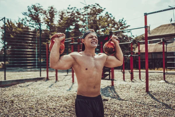 Athletic man working out with a kettlebell at street gym yard. Strength and motivation. — Stock Photo, Image