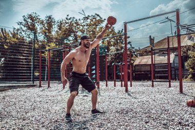 Atletizm adamı sokak spor salonunda bir kettlebell ile çalışıyor. Güç ve motivasyon.