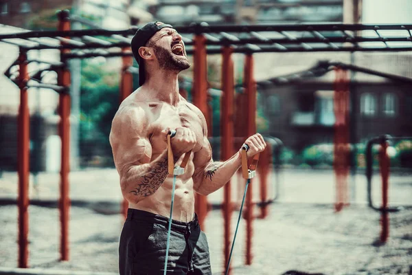 Fitness man exercising with stretching band in outdoor gym.