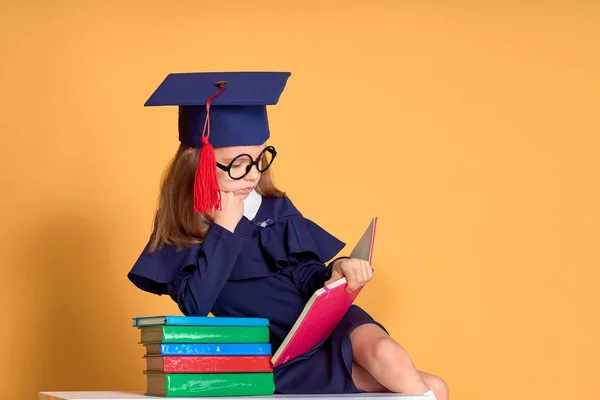 Curious schoolmeisje in afstuderen outfit studeren met studieboeken — Stockfoto