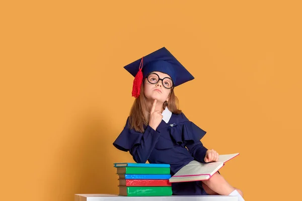 Curious schoolmeisje in afstuderen outfit studeren met studieboeken — Stockfoto