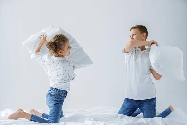 Vilains jumeaux fille et garçon amical combats mis en scène une bataille d'oreillers sur le lit dans la chambre . — Photo