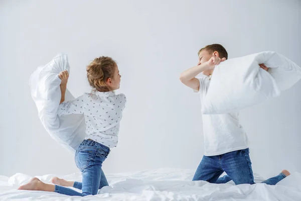 Ondeugende tweeling meisje en jongen vriendelijke gevechten geënsceneerd een kussengevecht op het bed in de slaapkamer. — Stockfoto