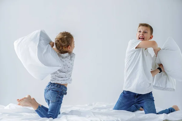 Travieso gemelos chica y niño amistoso lucha puesta en escena una pelea de almohadas en la cama en el dormitorio . —  Fotos de Stock