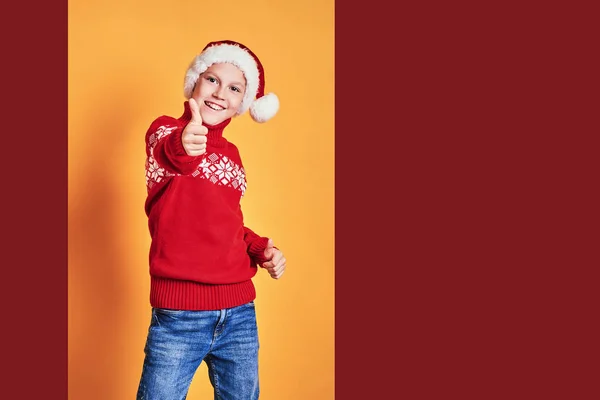 Niño en Santa sombrero mostrando pulgares hacia arriba en amarillo —  Fotos de Stock
