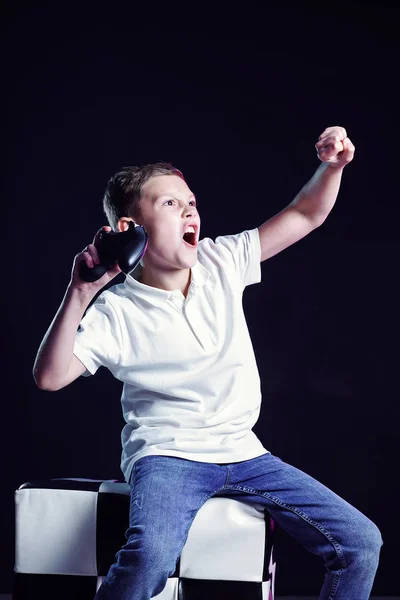 Niño feliz con la boca abierta y joystick gritando de alegría después de ganar en el videojuego sobre fondo negro — Foto de Stock
