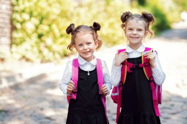 Okul sırt çantası giyen iki Gülen öğrenci kız. İlkokulun dışındaki mutlu Beyaz genç kızın portresi. Kameraya bakan gülümseyen kız öğrenci.