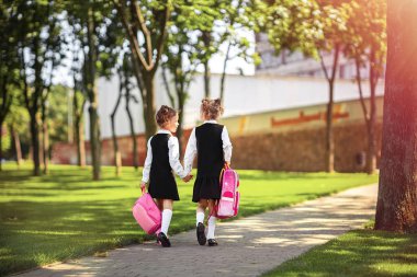 İlkokulun dışında okul sırt çantası giyen mutlu Beyaz genç gülümseyen kızların portresi. Derslerden sonra çocuklar eve gidiyor. Çalışmanın sonu. Yaz