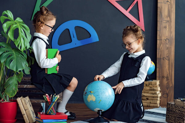 Smart girls reading books and examining globe in school