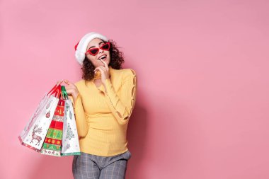 Güzel kadınlar parlak Noel renkli alışveriş çantaları taşırken giyiyor. Pembe arka plan. Noel alışveriş ve mutlu yeni yıl.