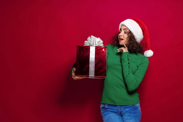 Beautiful fashion woman in santa claus hat. Warm Christmas sweater holding gift box on. — Stock Photo, Image