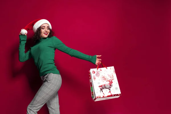 Hermosa mujer de moda en sombrero de Santa Claus. vistiendo brillante Navidad llevando coloridas bolsas de compras. El concepto de la tienda de regalos y navidades — Foto de Stock