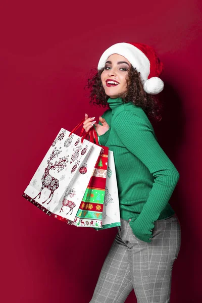Hermosa mujer de moda en sombrero de Santa Claus. vistiendo brillante Navidad llevando coloridas bolsas de compras. El concepto de la tienda de regalos y navidades — Foto de Stock