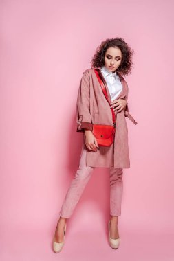 Pembe arka planda poz ceket ve çanta Mutlu kıvırcık esmer kız