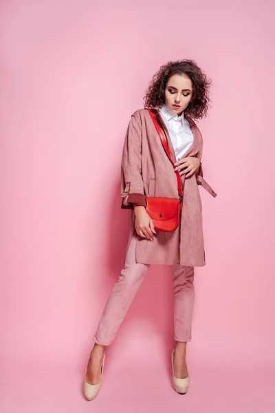Lycklig Lockig brunett flicka i päls och väska poserar på rosa bakgrund — Stockfoto