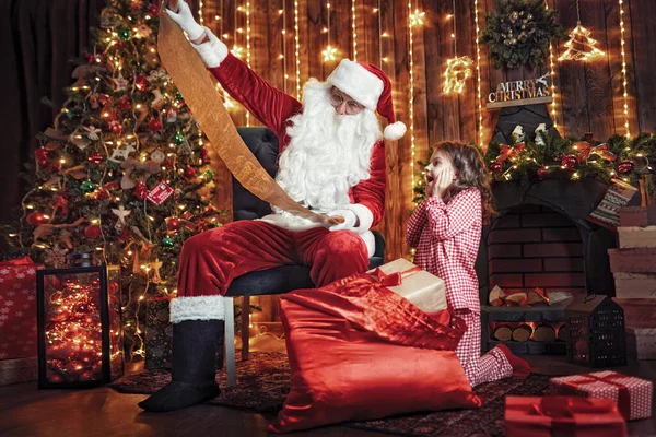 Père Noël avec petite fille mignonne étonnée en pyjama emballage cadeaux — Photo