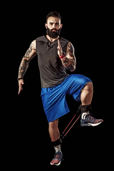 Giovane atleta accovacciato esercizio con fascia di resistenza intorno alle gambe. Lunghezza totale del corpo su sfondo nero dello studio . — Foto Stock