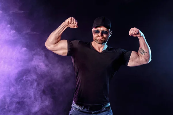 Young strong man bodybuilder in cap on wall background. Dark dramatic colors. — Stock Photo, Image