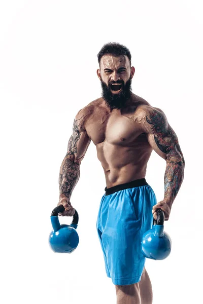 Muscular bodybuilder guy doing exercises with kettlebells over white background — Stock Photo, Image