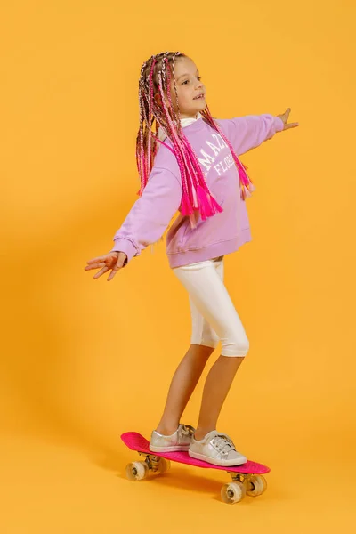 アクティブ若いです女の子でピンクシャツとホワイトショートパンツ保持スケートボード上の黄色の背景 — ストック写真