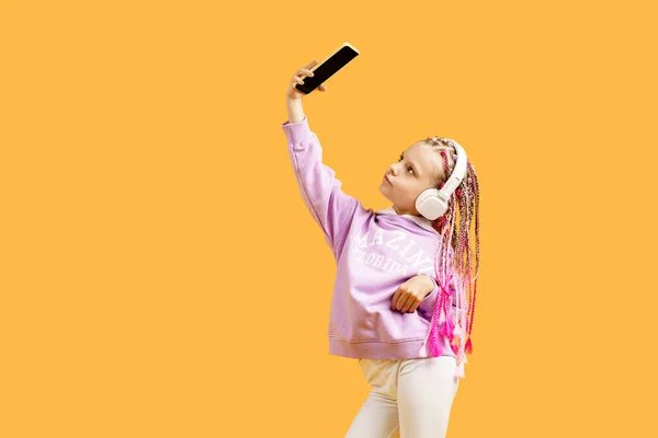かなり現代的な女の子とともにピンクのドレッドロックでヘッドフォン笑顔と作ります自画自画撮りスマートフォン隔離上の黄色 — ストック写真