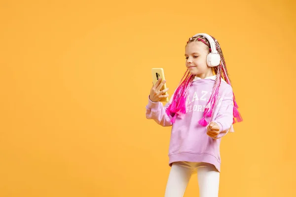 Pretty modern girl with pink dreadlocks in headphones smiling and making selfie on smartphone isolated over yellow — Stock Photo, Image