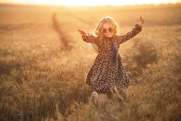 Mode foto av en liten flicka i leopardprint klänning, solglasögon och halm hatt på kvällen vete fält — Stockfoto