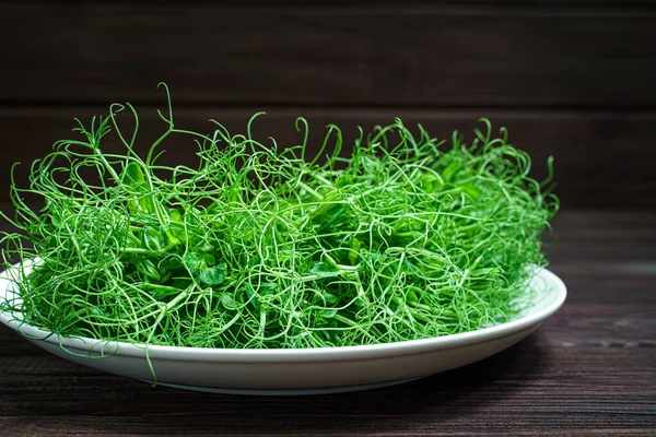 Свежая горох микрозеленые ростки на тарелке на деревянной поверхности — стоковое фото
