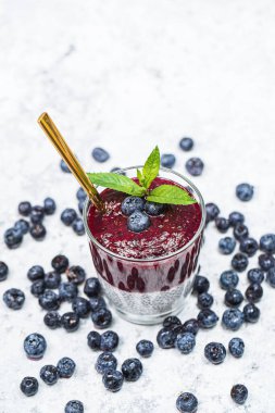 Beyaz taş arka planda chia tohumları ve yaban mersinli sağlıklı kahvaltı, vejetaryen gıda, diyet ve sağlık konsepti