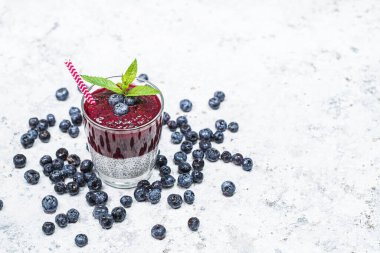 Beyaz taş arka planda chia tohumları ve yaban mersinli sağlıklı kahvaltı, vejetaryen gıda, diyet ve sağlık konsepti