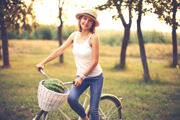 Bella ragazza sorridente in cappello di paglia con bicicletta nel parco — Foto Stock