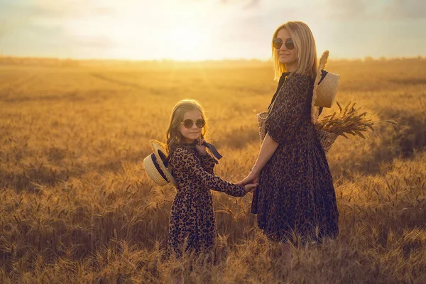 Jovem mãe e sua filha no campo de trigo em um dia ensolarado — Fotografia de Stock