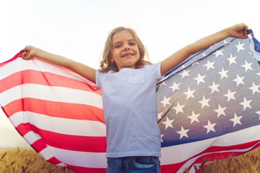 Güzel bir buğday tarlasında Amerikan bayrağı takan sevimli vatansever kız.