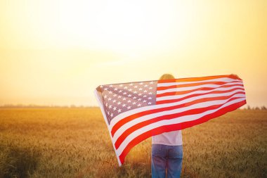 Buğday tarlasında koşan ve kaygısız bir kadın Amerikan bayrağını taşıyor.