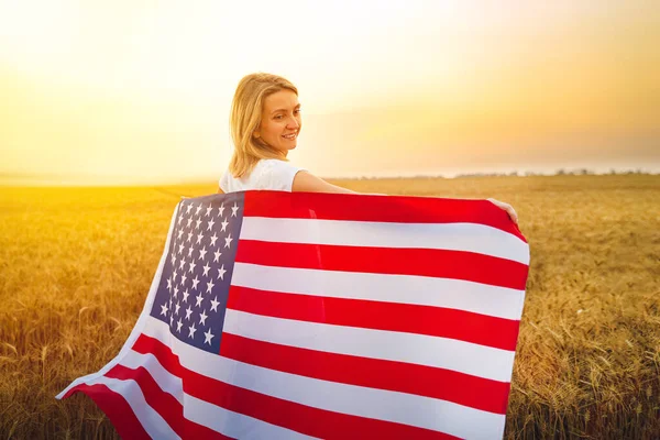 Kvinna kör och hoppa bekymmersfri med öppna armar över vetefält Holding USA flagga — Stockfoto
