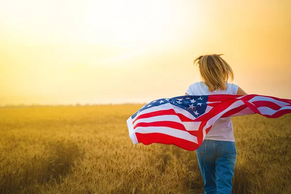 Mulher correndo e saltando despreocupado com os braços abertos sobre o campo de trigo Segurando bandeira dos EUA — Fotografia de Stock