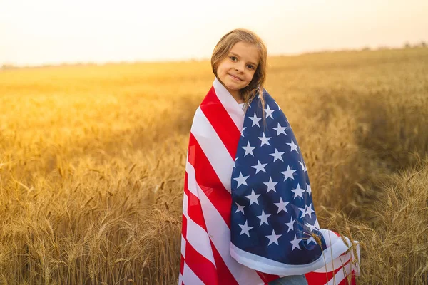 Rozkošná vlastenecká dívka s americkou vlajkou v krásném pšeničném poli — Stock fotografie